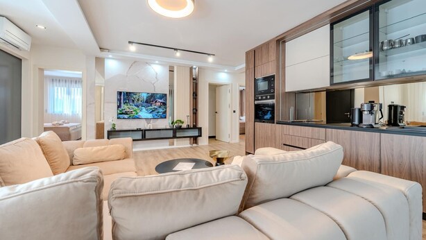 Un salon moderne comprenant un canapé, une table basse et un téléviseur. Il y a également un coin cuisine avec des placards et un four à micro-ondes.