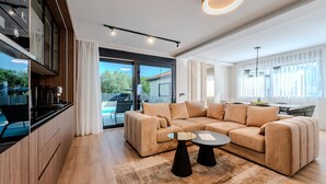 Un salon moderne avec un canapé d’angle beige, une table basse et un coin cuisine doté d’un four encastré.