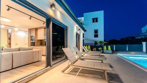 Une maison moderne dotée d’une piscine, d’un espace salon extérieur et d’une terrasse bien éclairée.