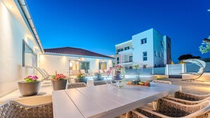 Une terrasse extérieure avec une table et des chaises, des plantes en pot et un bâtiment moderne en arrière-plan.