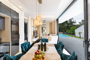 Een moderne eethoek met een lange tafel, teal stoelen en een fruitmand als decoratie.
