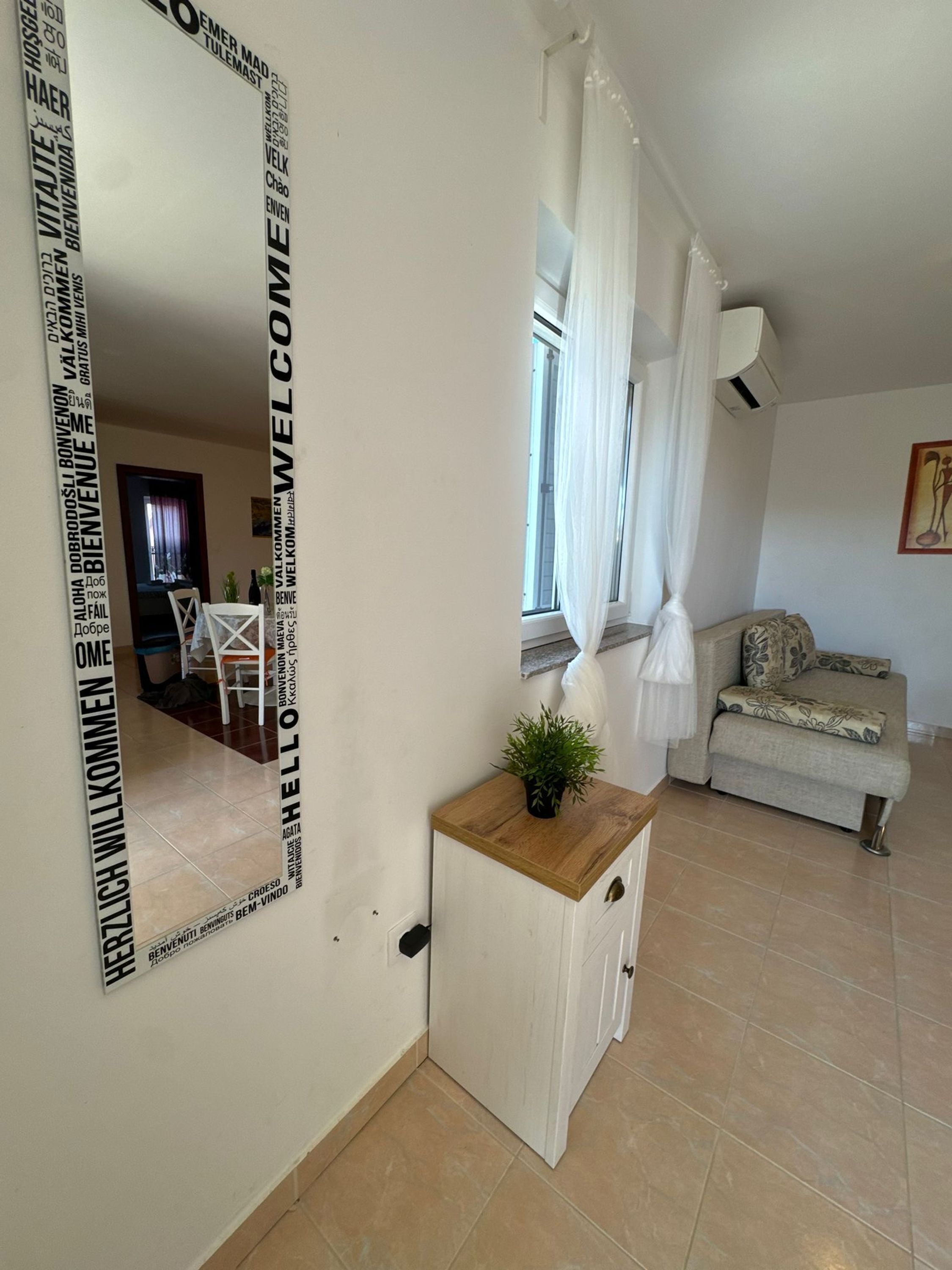 A modern living room with a large mirror, a sofa, a small table with a plant, and a window with curtains.