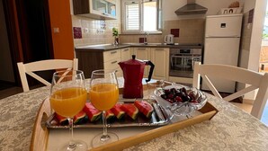 A dining area with a table set for two, featuring a tray with two glasses of orange juice, watermelon slices, and a bowl of cherries. - Beautiful Apartment Bodulo 3 (Povljana)