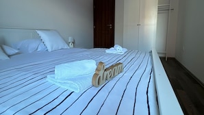 A neatly made bed with striped bedding, a wooden 'dream' sign, and a white wardrobe in a simple, clean room. - Beautiful Apartment Bodulo 3 (Povljana)