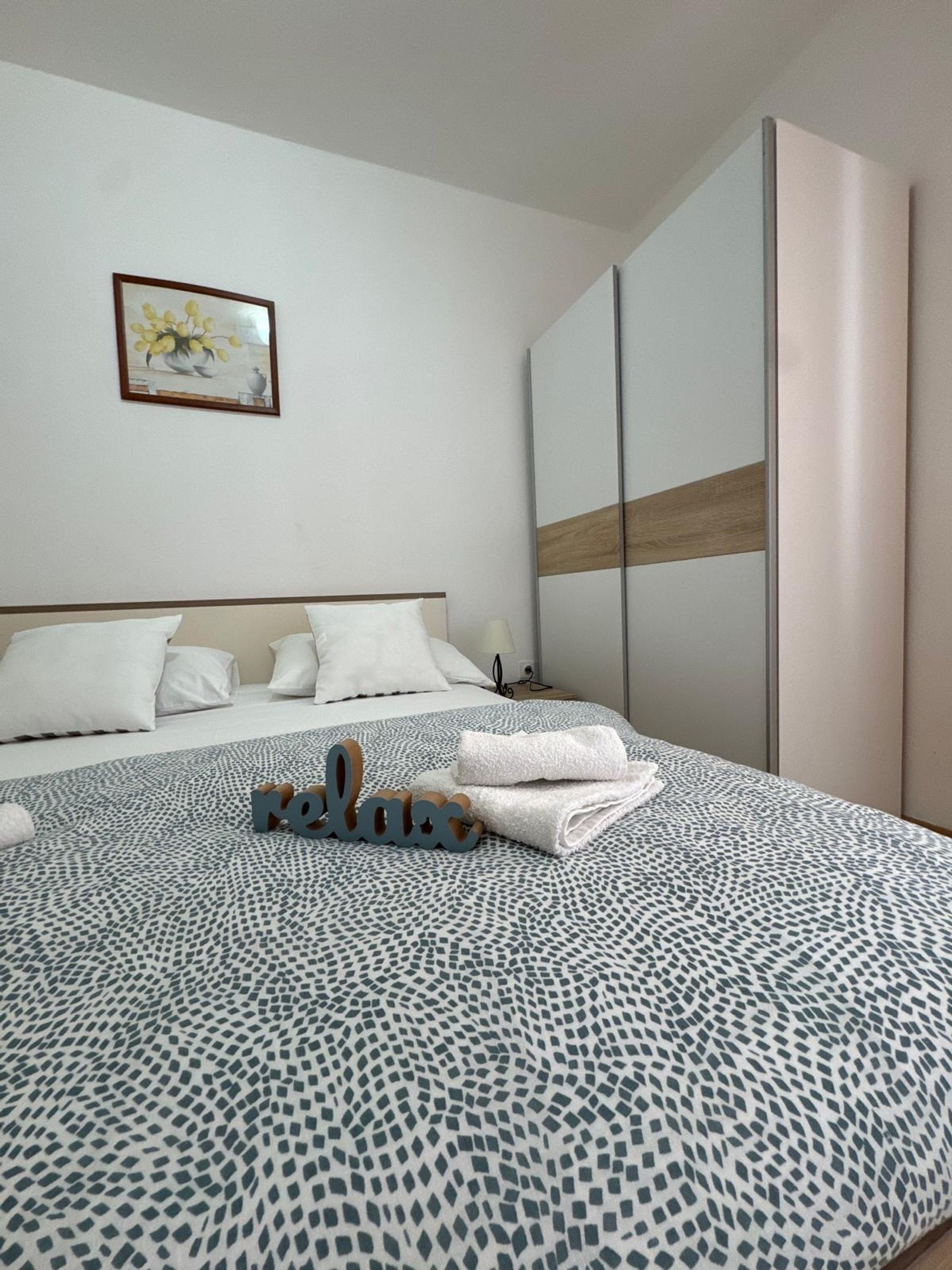 A neatly made bed with a patterned bedspread, a bedside table with a lamp, and a framed picture on the wall.