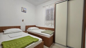 Een slaapkamer met twee bedden, houten hoofdborden, een groene handdoek, een schilderij en een schuifdeur.
