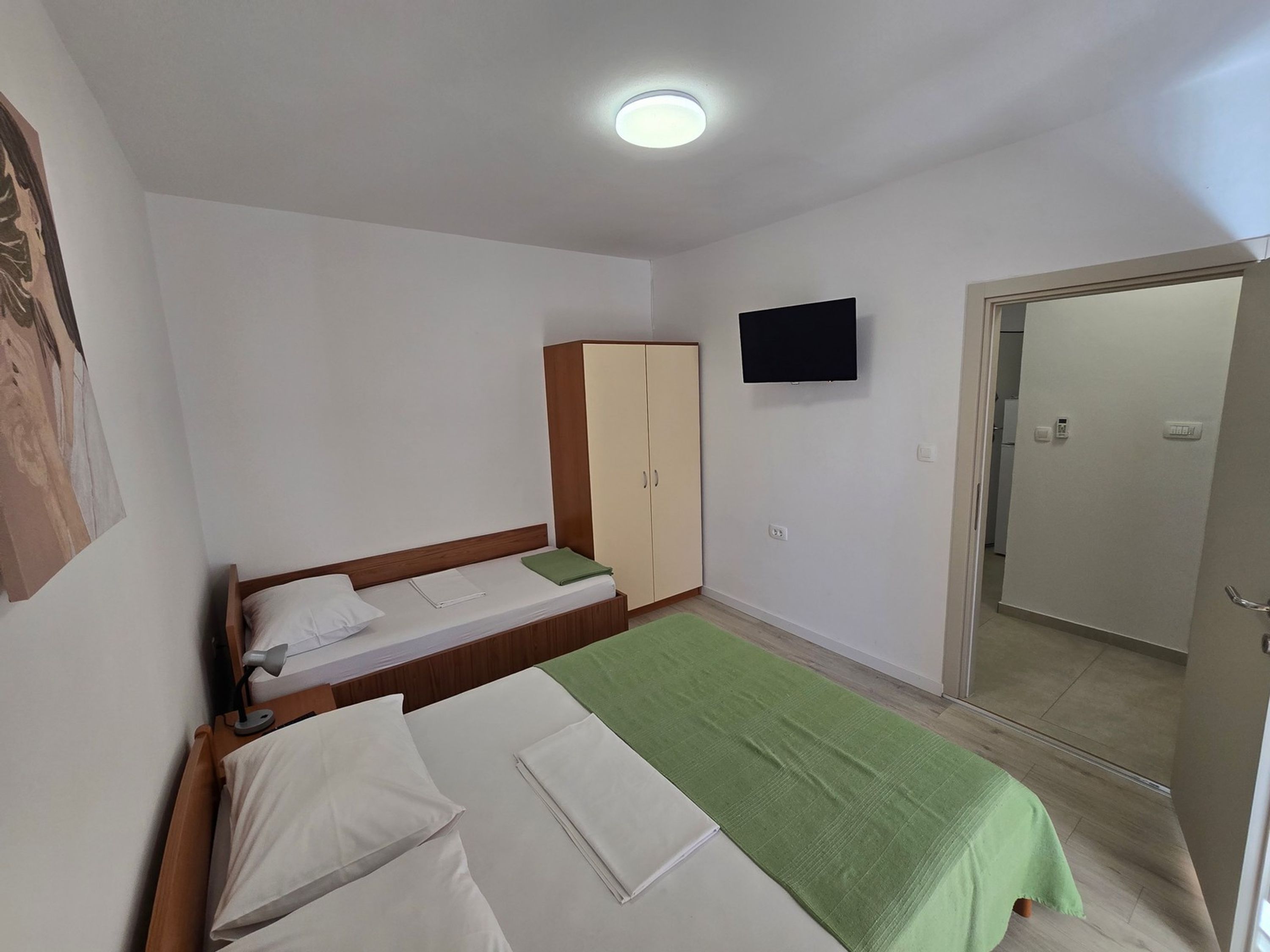 A room with two beds, a wardrobe, a television, and a door leading to another room.