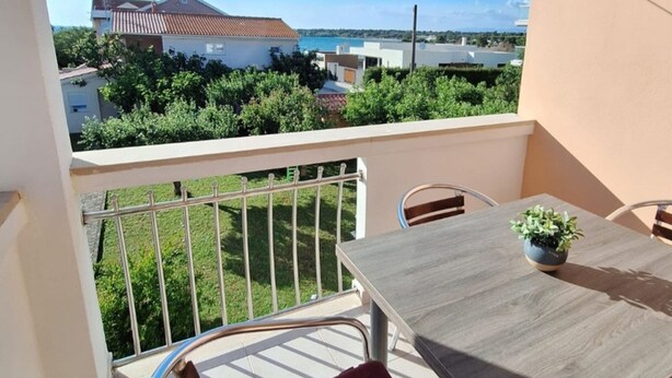 Een balkon met een tafel en stoelen, een plant in pot en een uitzicht op gebouwen en groen.