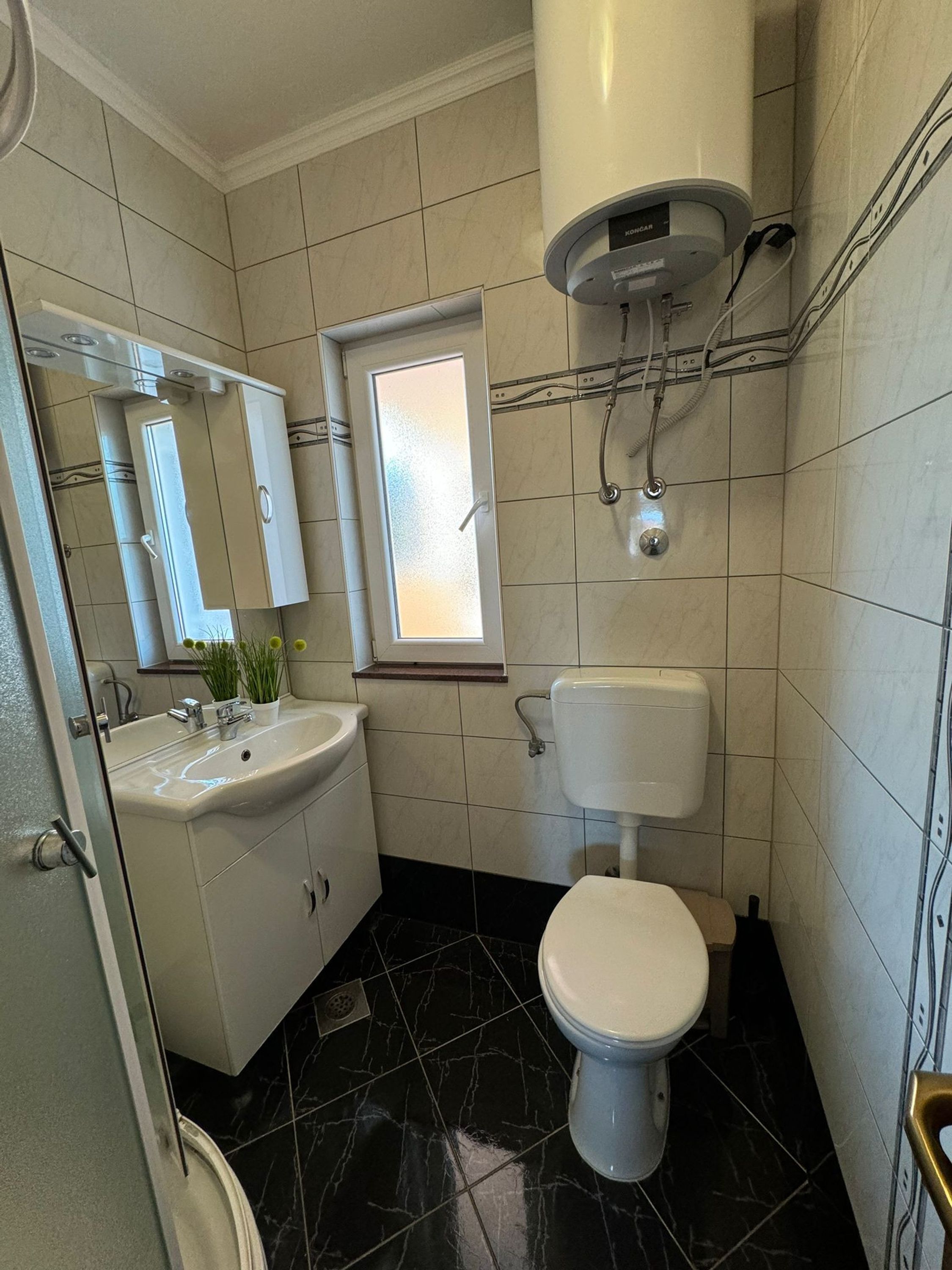 A bathroom with a toilet, sink, mirror, and window.