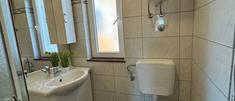 A bathroom with a toilet, sink, mirror, and window.