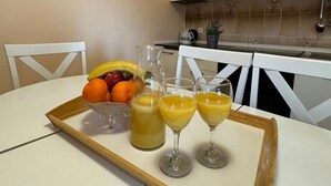 A kitchen with a white table, a fruit bowl, a pitcher, and two glasses of orange juice. - Beautiful Apartment Bodulo 1 (Povljana)