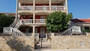 A multi-story building with a central staircase, balconies, and a stone wall surrounding the property. - Beautiful Apartment Bodulo 1 (Povljana)