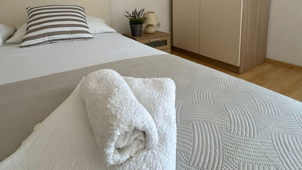 A neatly made bed with a white blanket, a striped pillow, and a small bedside plant. - Beautiful Apartment Bodulo 1 (Povljana)
