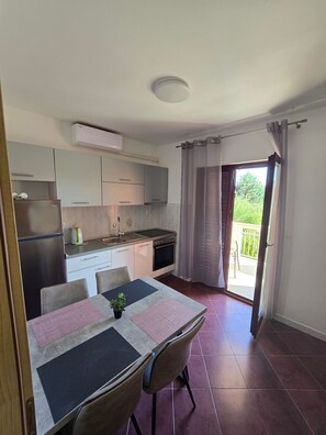 A compact kitchen with modern appliances, a dining table with chairs, and a view of a balcony with curtains. - Apartment Gina in Zaton (Nin)