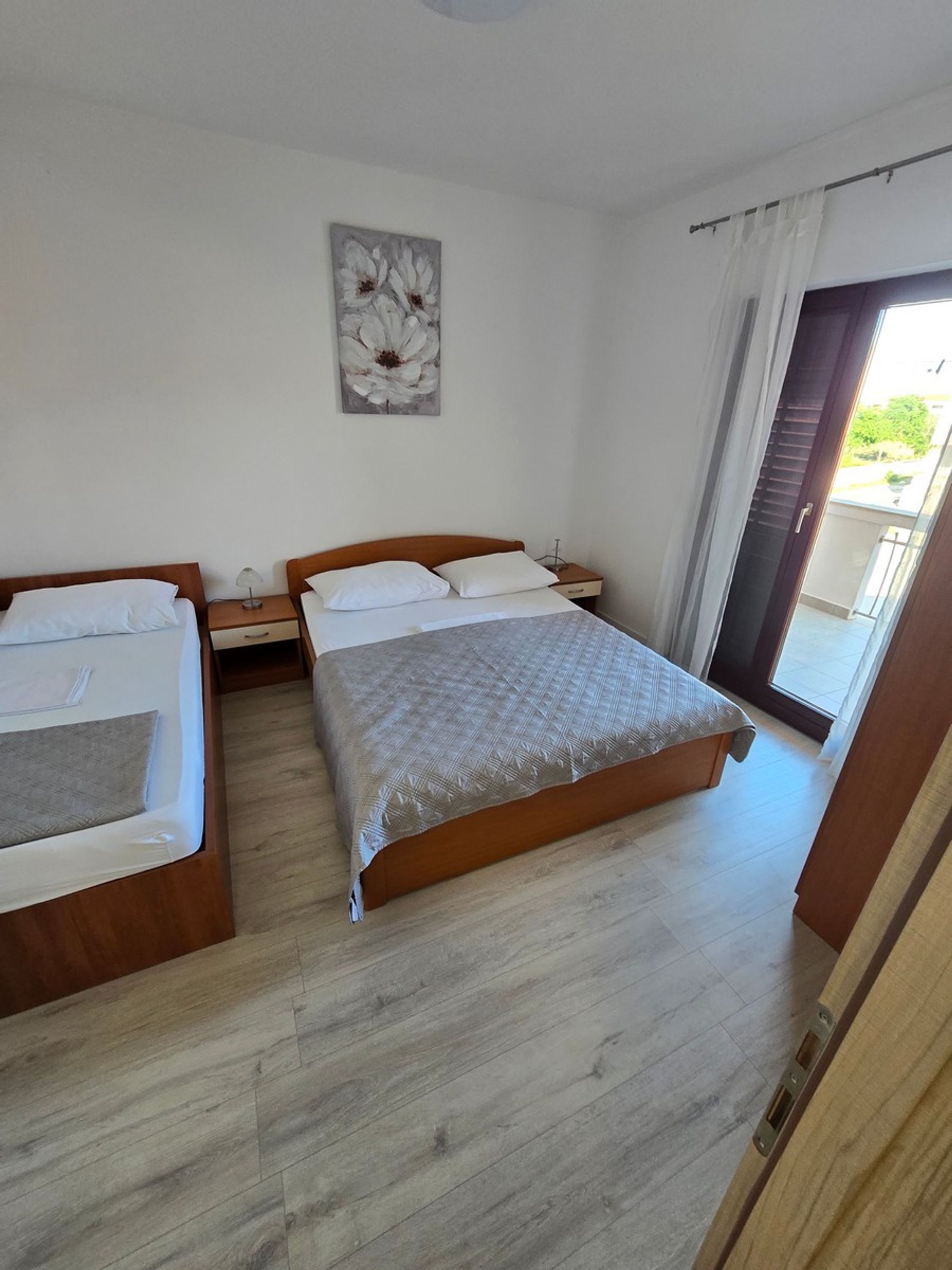 A bedroom with a large bed, a smaller bed, a nightstand, a lamp, and a painting on the wall.