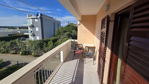 Un balcon avec une table et des chaises, une vue sur la rue et un immeuble en arrière-plan.