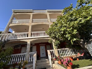 A multi-story building with a balcony on each floor, a front door, and potted plants. - Beautiful Apartment Bodulo 5 (Povljana)
