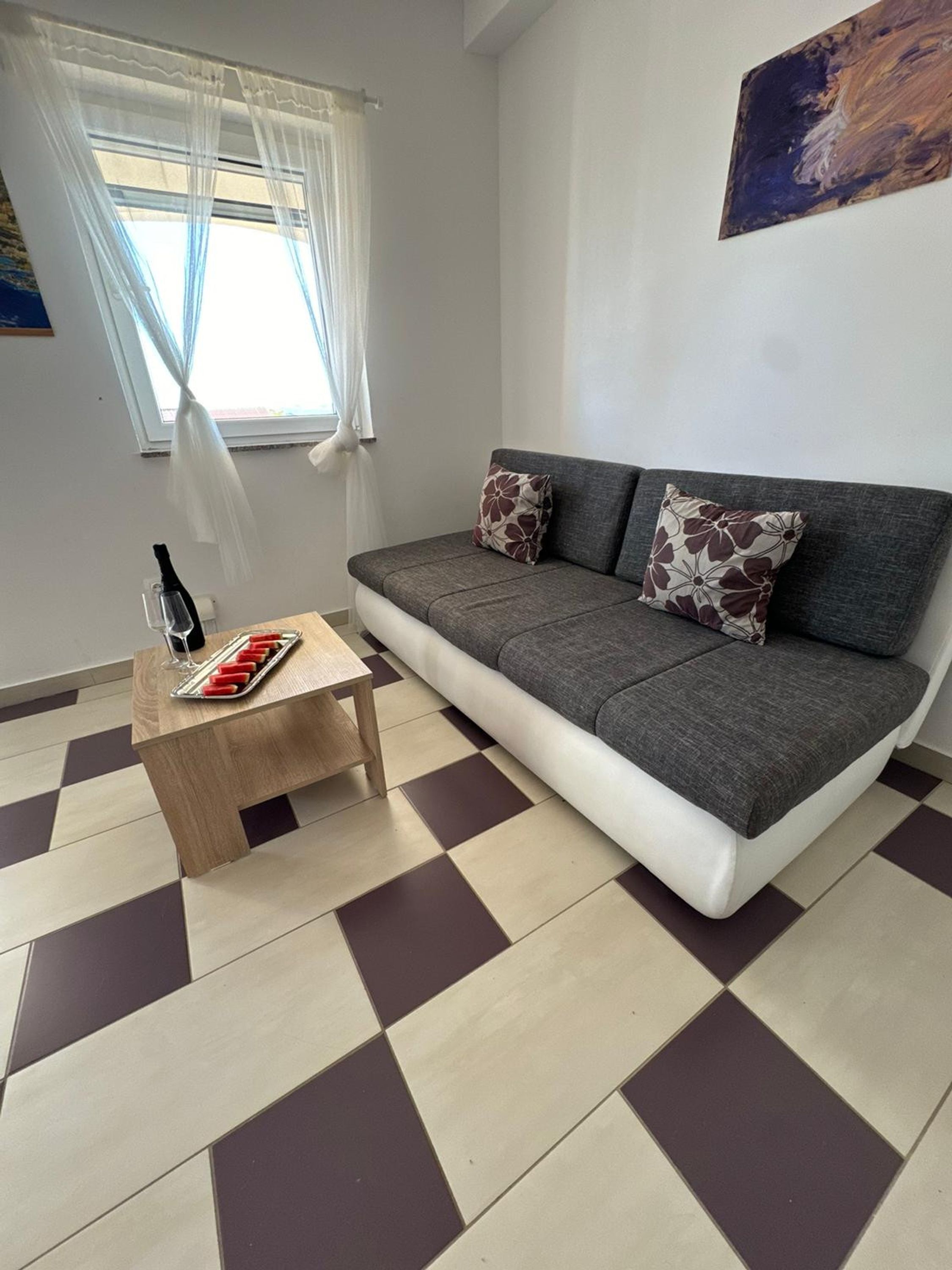 A modern living room with a grey sofa, patterned cushions, a wooden coffee table, and a checkered floor.