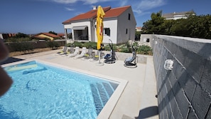 A swimming pool with lounge chairs and a hanging chair, surrounded by a stone wall and a house with a red roof. - Villa Pauliana in Povljana (Povljana)