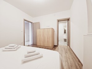A modern hotel room with a neatly made bed, a wooden wardrobe, and a bathroom visible through an open door. - Villa Pauliana in Povljana (Povljana)