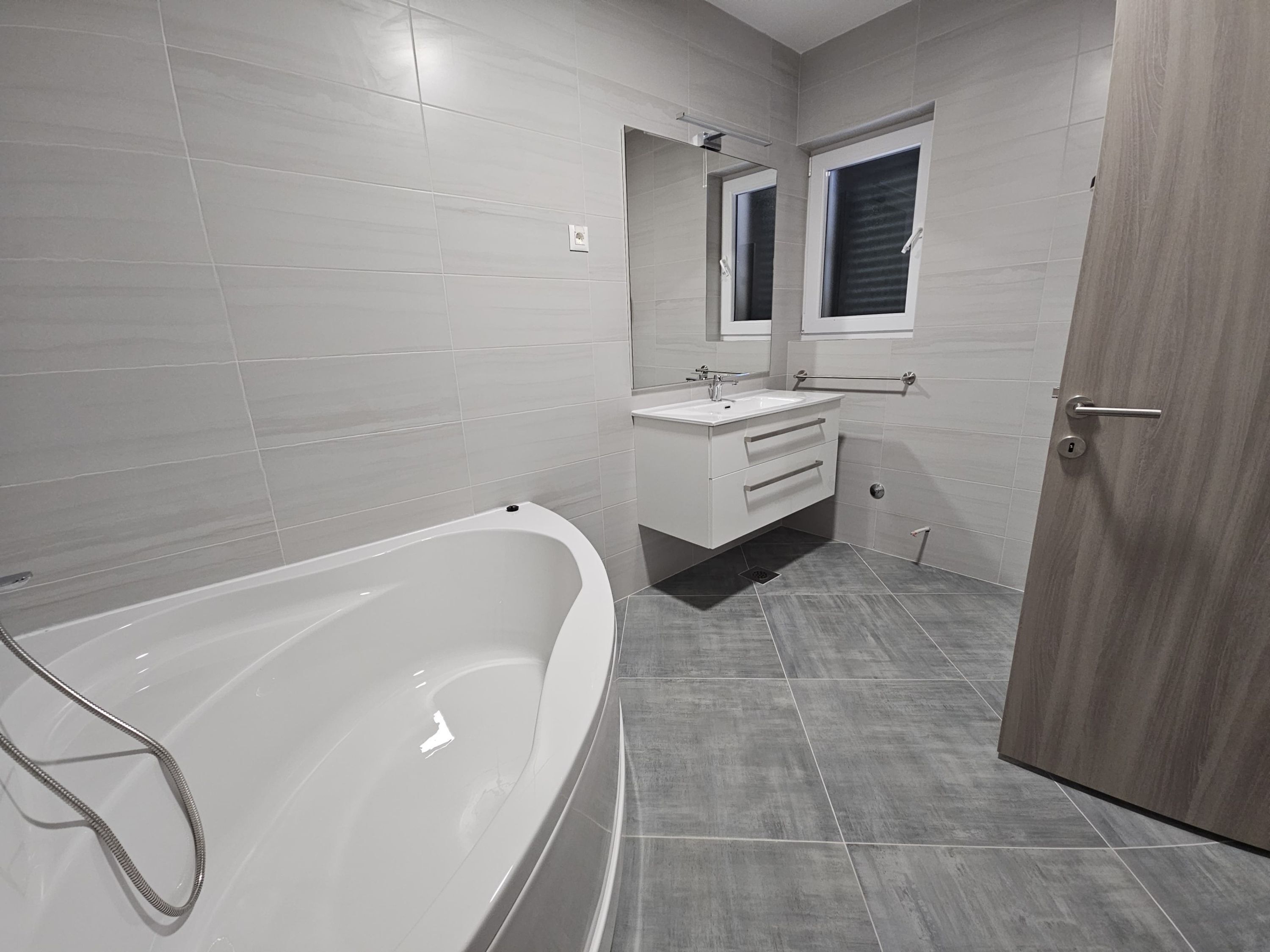 Een moderne badkamer met een vrijstaand bad, een wastafel met spiegel en een houten deur.