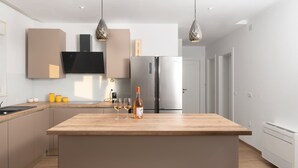Une cuisine moderne dotée d’un îlot central, d’appareils électroménagers en acier inoxydable, de luminaires suspendus et d’un téléviseur à écran plat fixé au-dessus de l’îlot.