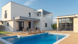 Une maison moderne à deux étages dotée d’une piscine, d’un espace salon extérieur et d’une véranda en verre.