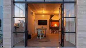 Un intérieur moderne avec une porte vitrée donnant sur un espace de vie comprenant une cheminée, un téléviseur fixé au mur et une table à manger avec des chaises.