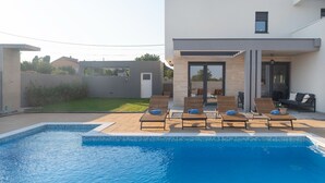 Un espace piscine moderne, doté de chaises longues et offrant une vue dégagée sur la piscine.