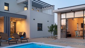 Une maison moderne dotée d’une piscine, d’un espace salon extérieur et d’une porte vitrée donnant sur une salle à manger.
