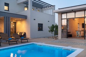 A modern house with a swimming pool, outdoor seating, and a glass door leading to a dining area. - Beautiful Villa Aria (Zadar)