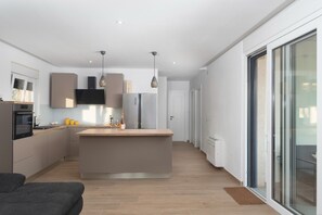 A modern kitchen with a central island, built-in appliances, pendant lighting, and a sliding glass door leading to a balcony. - Beautiful Villa Aria (Zadar)