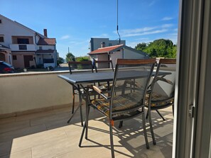 En balkon med et bord og stole, udsigt til huse og en klar himmel.