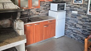 A compact kitchen with wooden cabinets, a stone wall, a microwave, and a built-in grill. - Apartment Marcela in Zaton (Nin)