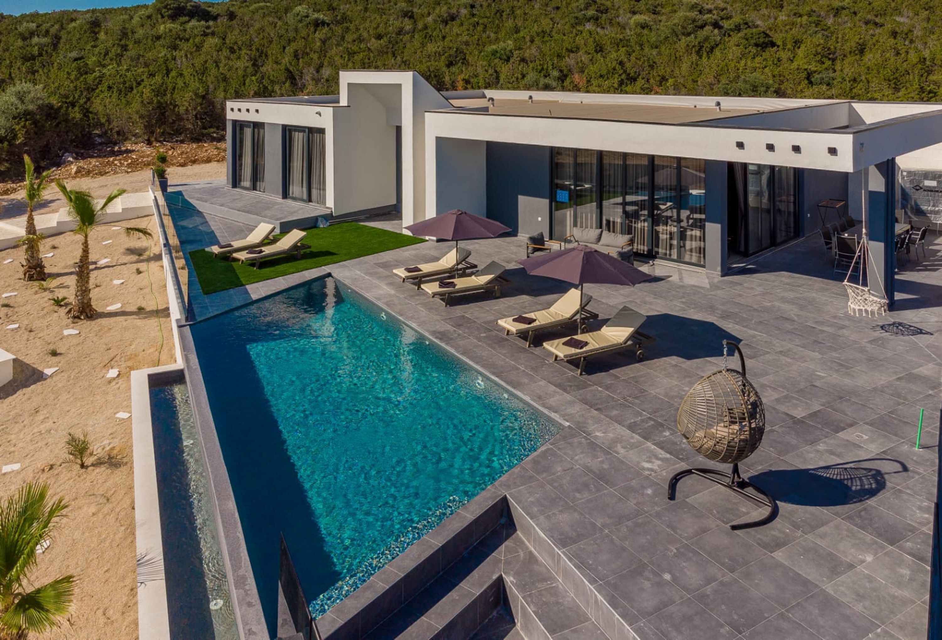 A modern poolside area with a clear blue pool, lounge chairs, and umbrellas.