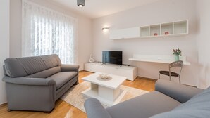 Un soggiorno moderno con un divano grigio, un tavolino da caffè bianco, una TV a schermo piatto e una base televisiva bianca con ripiani.