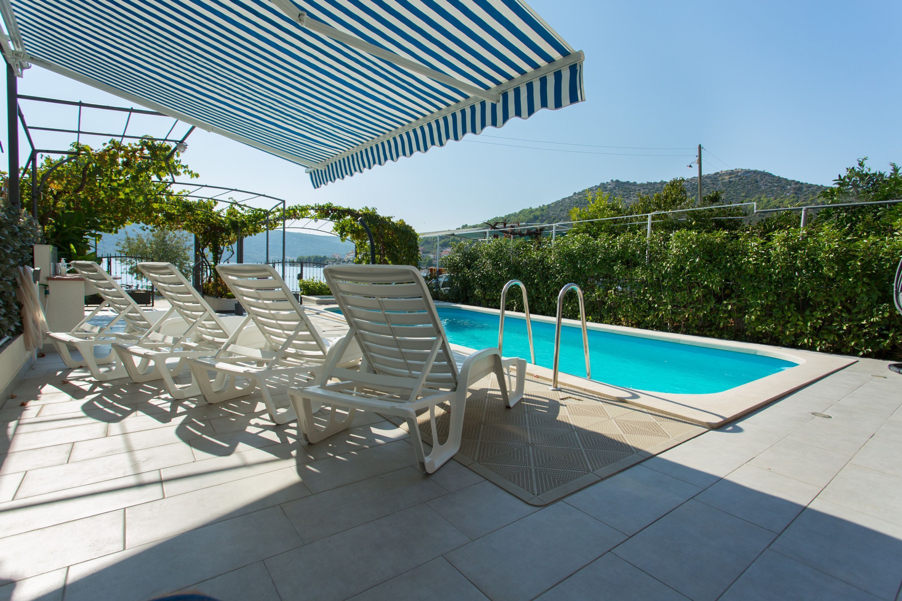 Un área de piscina con sillones de descanso y una zona de estar cubierta.