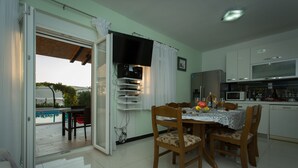 Spiseområde med et bord til fire, et køkken med moderne hårde hvidevarer og en skydedør til en udendørs terrasse.
