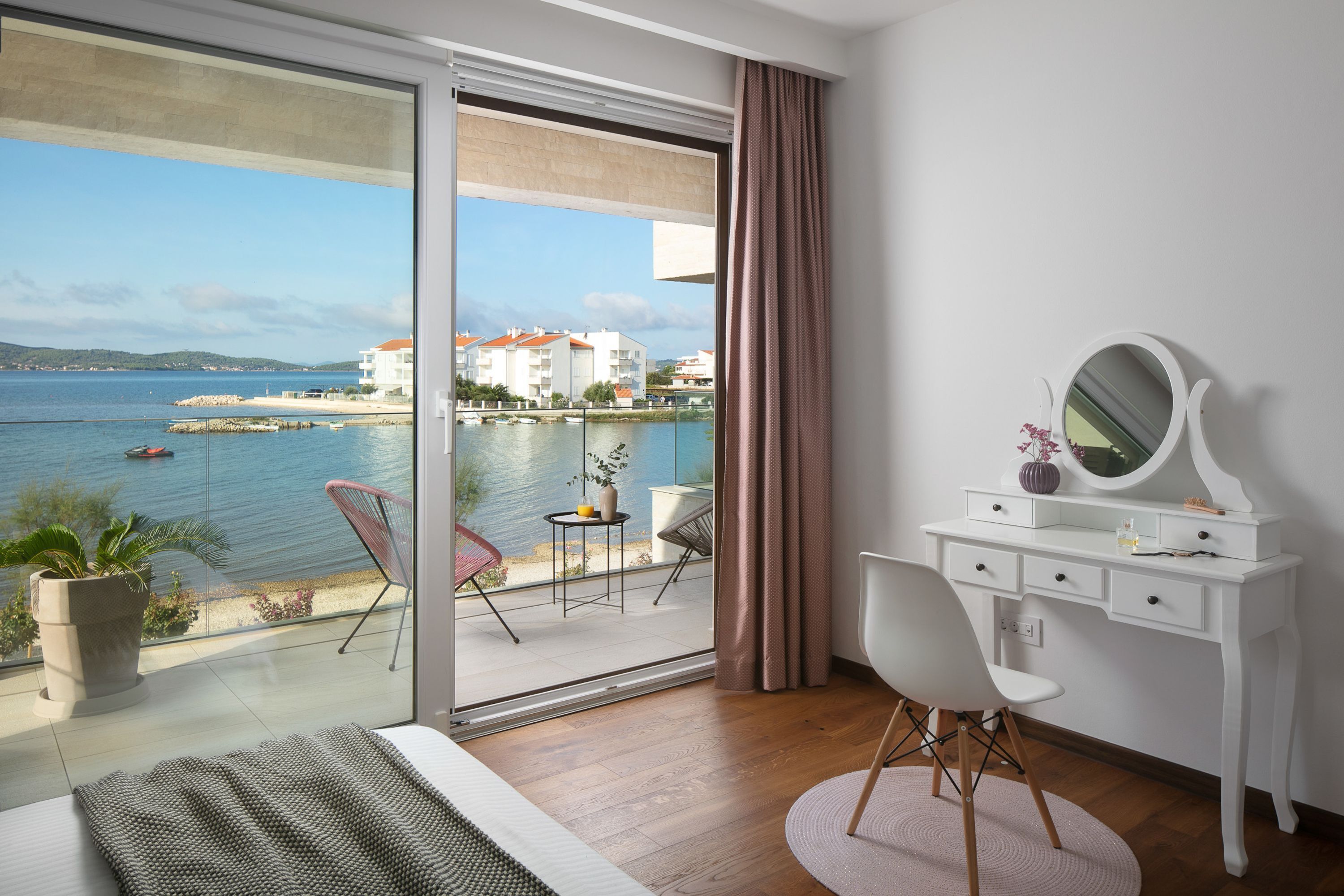 Quarto com uma grande porta de vidro deslizante que dá para uma varanda com vista para o mar e edifícios.