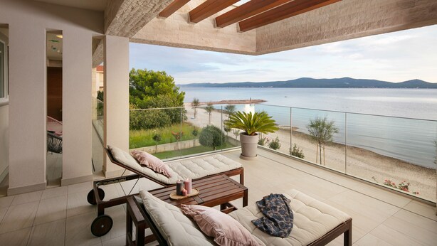 A balcony with a view of the sea, a lounge area with a table and chairs, and a potted plant. - Beautiful Villa Sale (Sukosan)