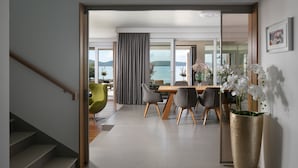 A modern dining area with a view of the sea, a large vase of white flowers, and a staircase leading to another room. - Beautiful Villa Sale (Sukosan)