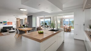 A modern kitchen with a central island, dining area, and a view of the sea. - Beautiful Villa Sale (Sukosan)
