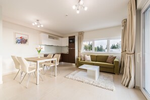 Ein modernes Wohnzimmer mit Essbereich, einem grünen Sofa und einer Küche im Hintergrund.
