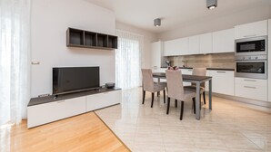 A modern kitchen with white cabinets, a built-in oven, and a dining area with a table and chairs. - Sargas Suite 3 With Pool View (Novalja)