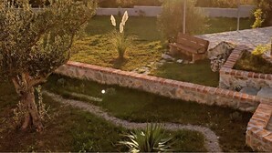A landscaped garden with a stone pathway, a tree, and a view of distant hills. - Family Home Iskra in Bulic (Benkovac)