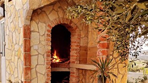 A stone fireplace with a fire burning inside, surrounded by potted plants and a stone pathway. - Family Home Iskra in Bulic (Benkovac)
