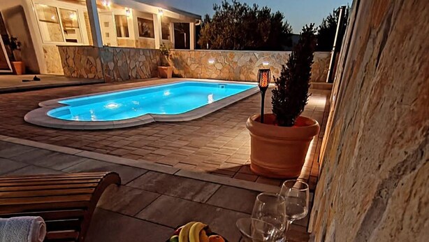 A poolside area with a lounge chair, a fruit bowl, and a glass of wine on a table. - Family Home Iskra in Bulic (Benkovac)
