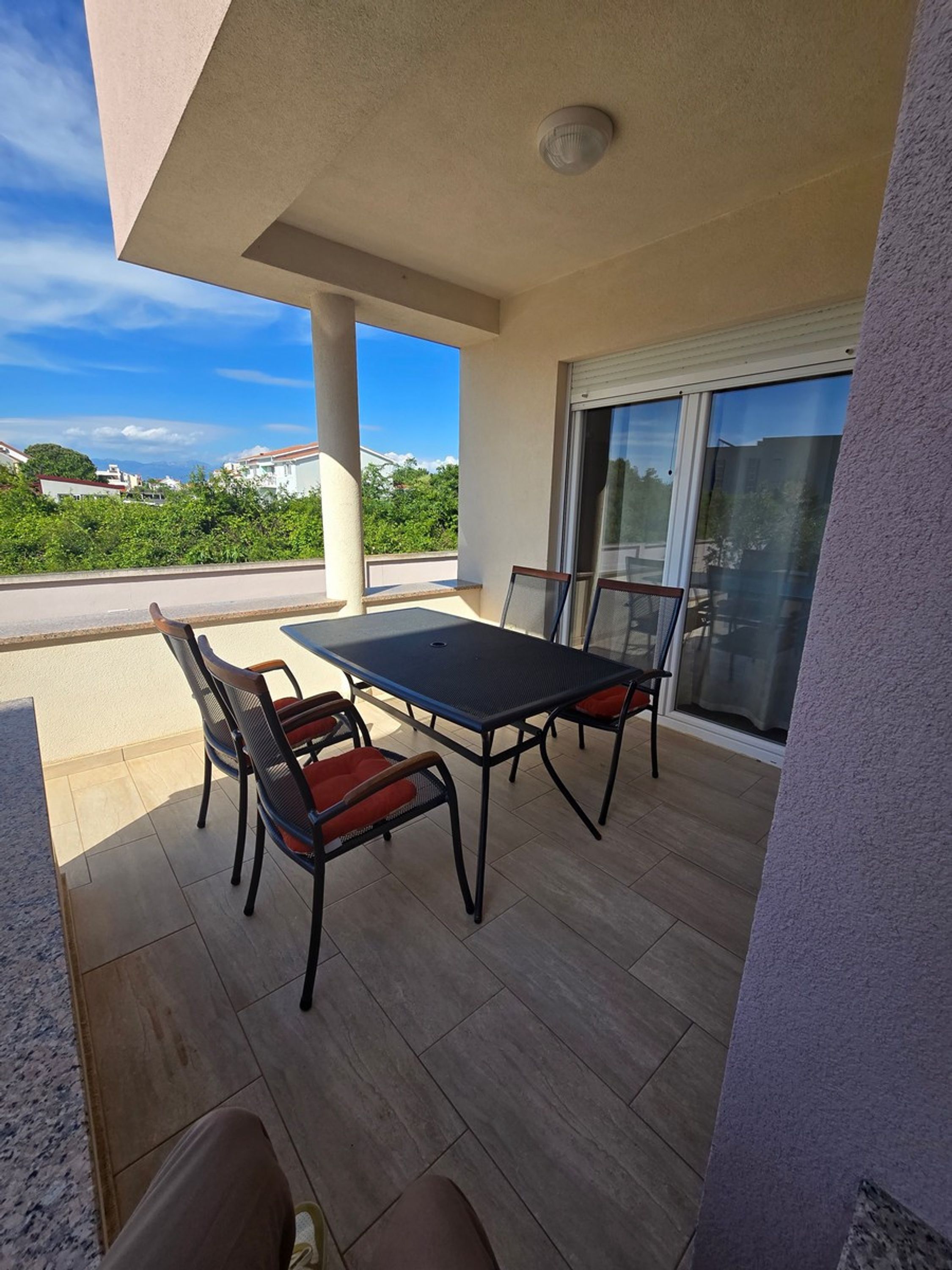 Une terrasse couverte avec une table et des chaises, une porte-fenêtre coulissante et une vue sur les environs.