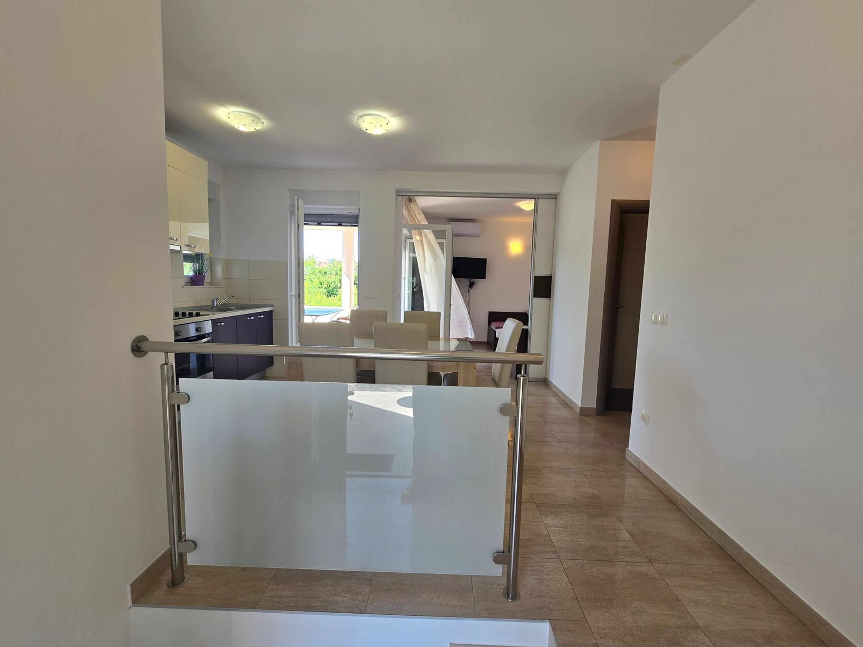 A modern apartment with a kitchen, dining area, and a balcony with a glass railing.