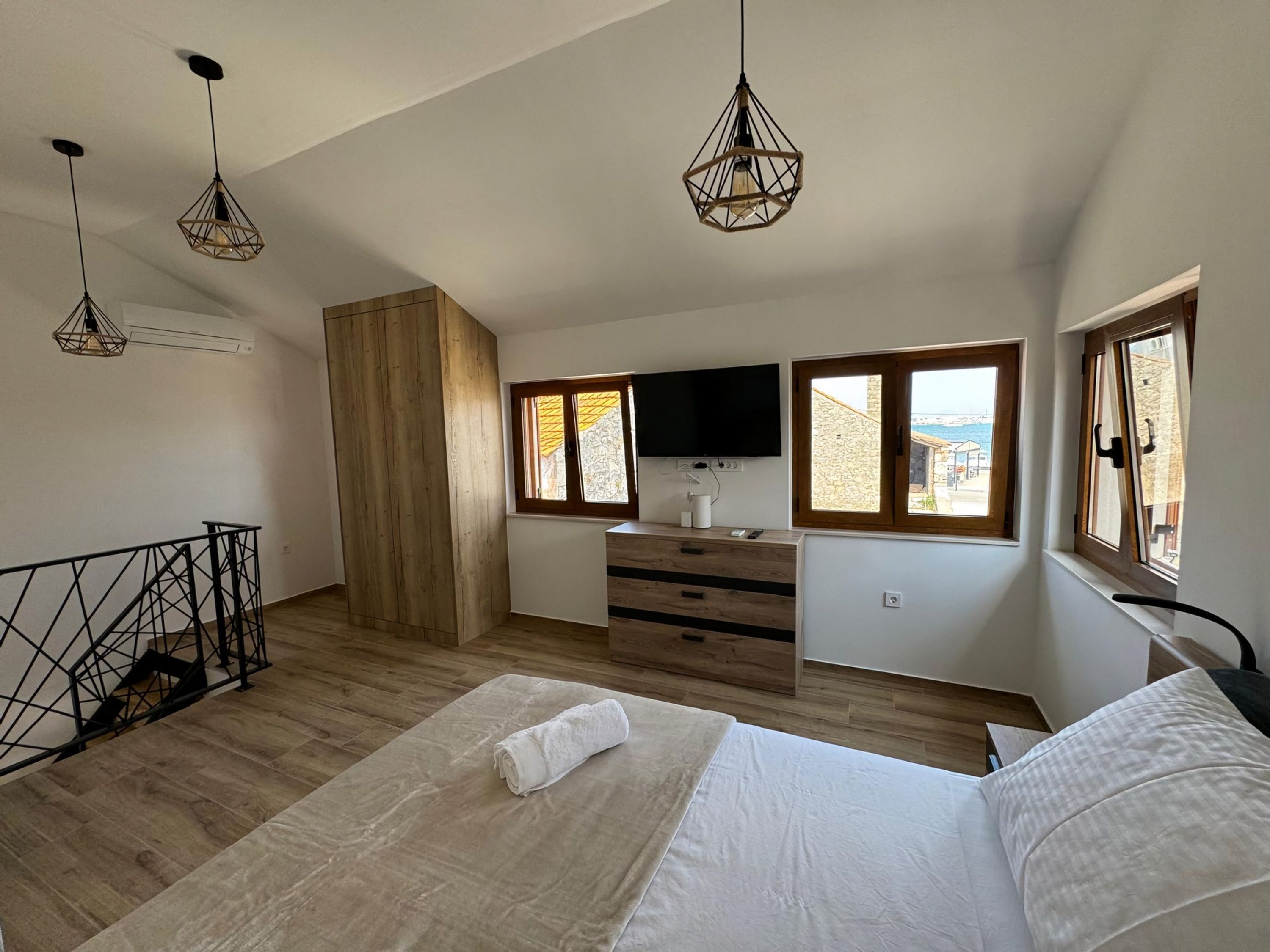 A bedroom with a bed, wooden wardrobe, TV, and windows with a view.